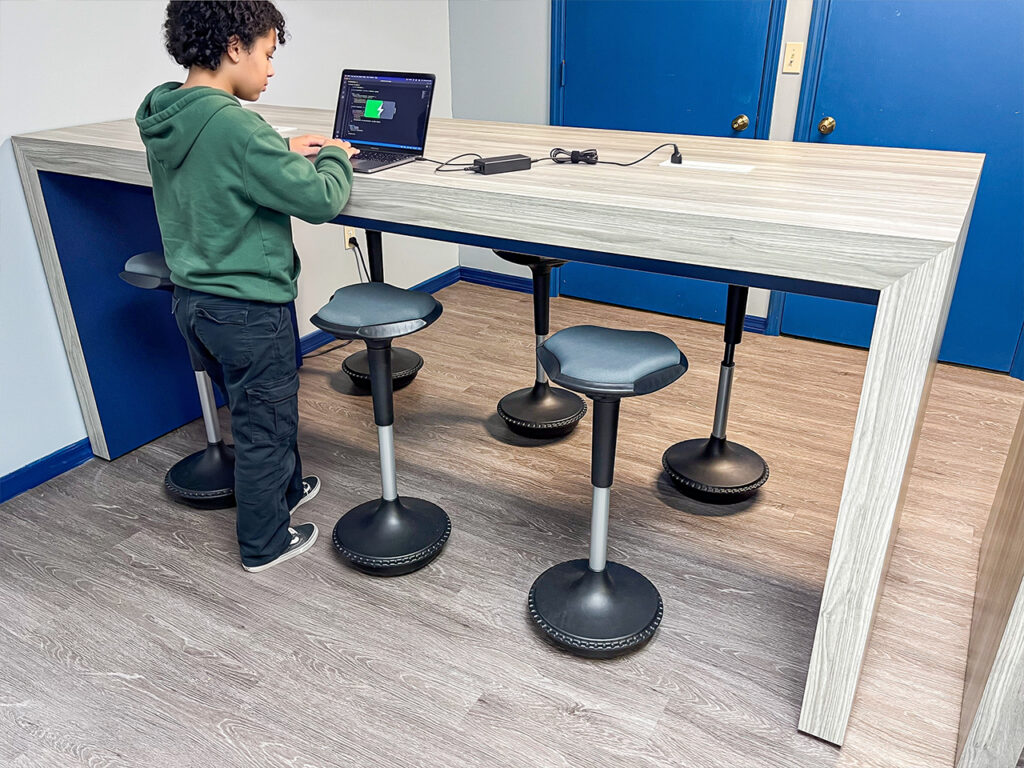 Device charging station in a school library featuring a powered SHARE table and RKR stools.